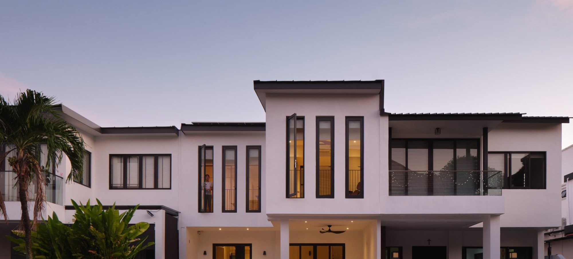 The renovated terrace house at dusk, its tall slot windows glowing warmly