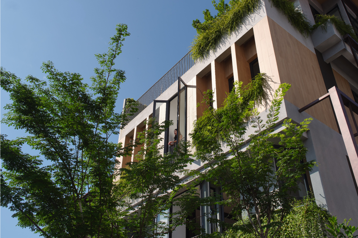 Upward view of the planted facade with a figure on a balcony framed by deep concrete fins